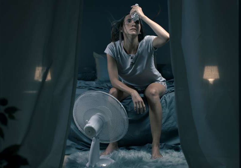 woman sitting on bed in front of a fan hot flash feat ss
