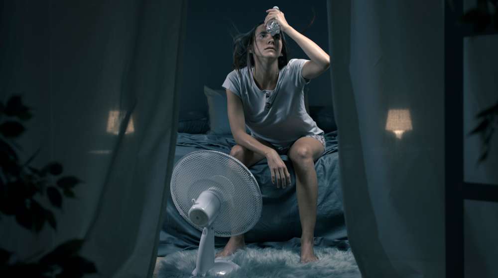woman sitting on bed in front of a fan hot flash feat ss