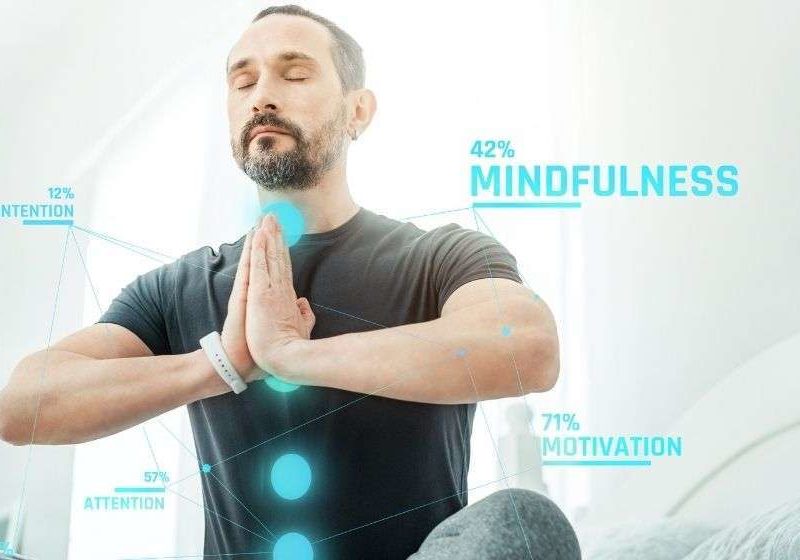 Pleasant calm beardful man sitting on the bed closing eyes and meditating | feature | Biohacking: Improve Your Well-being With Simple Health ?Hacks?