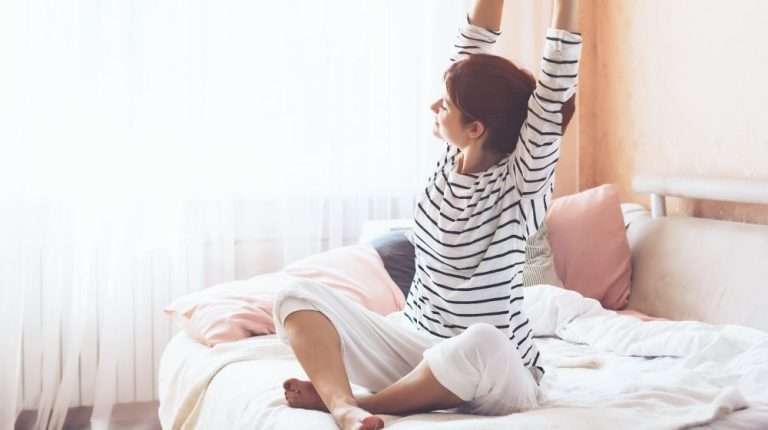 a woman sketching her arms on the bed in the morning | Feature | How to Have More Energy In the Morning