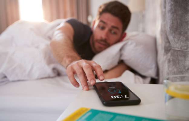 the man turns off the alarm on phone  Avoid Hitting Snooze  How to Have More Energy In the Morning