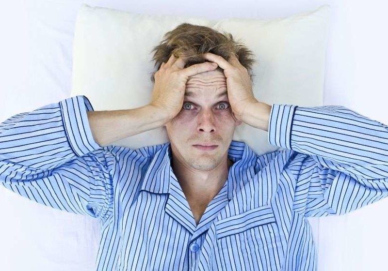a-tired-man-wearing-pajama-is-holding-his-head | Feature | Sleep Loss Exacerbates Inflammatory Markers in Rheumatoid Arthritis Patients