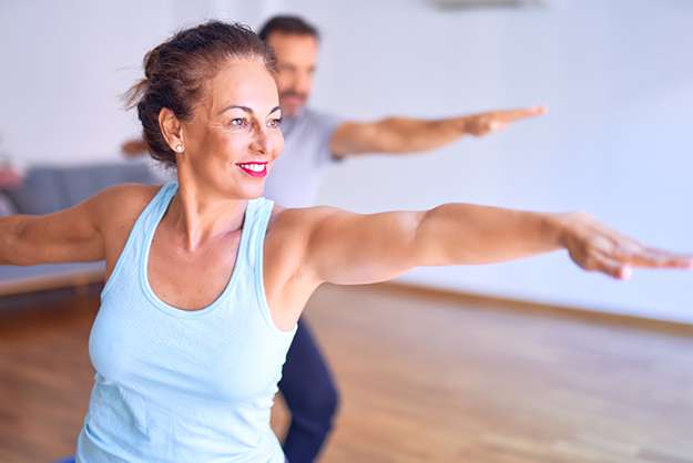 [How to Prevent Neurodegeneration] Middle age beautiful sporty couple smiling happy. Standing with smile on face practicing yoga doing warrior pose at gym_SS_