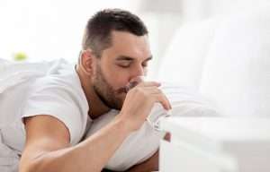 man-in-bed-drinking-from-glass-of-water-at-home-ss-body