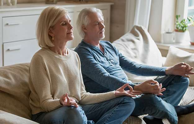 Calm-senior-middle-aged-couple-practicing-yoga-together-sitting-in-lotus-pose-on-sofa---What-to-Do-if-We-Don’t-Get-Sleep-Erection