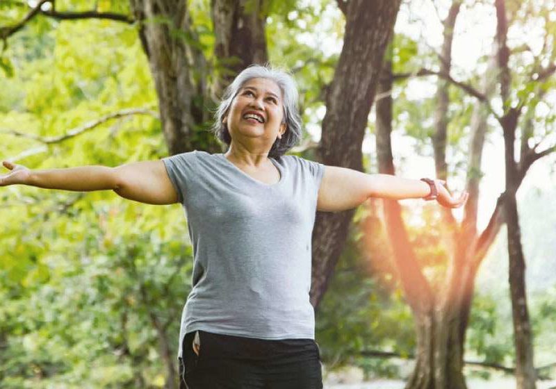 Smiling older woman with arms outstretched in the park