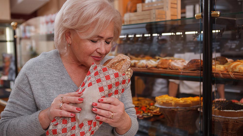 Lovely-senior-lady-buying-fresh-bread-at-local-bakery-store-smelling-tasty-fresh-loaf-of-bread-How-to-Control-Menopause-Hunger