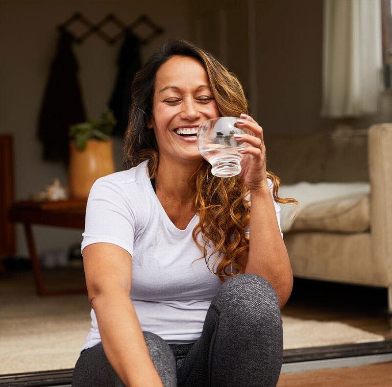 woman smiling and drinking water after starting hormone therapy