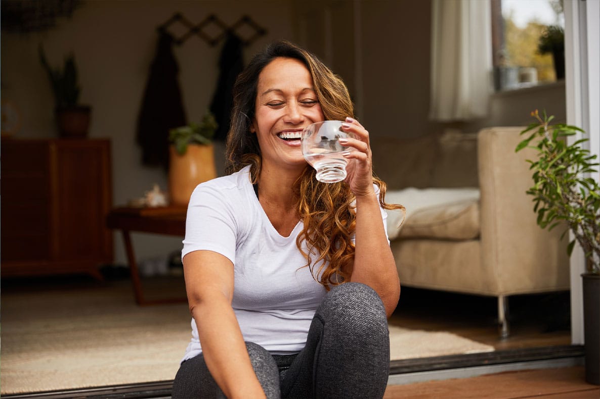 woman smiling and drinking water after starting hormone therapy