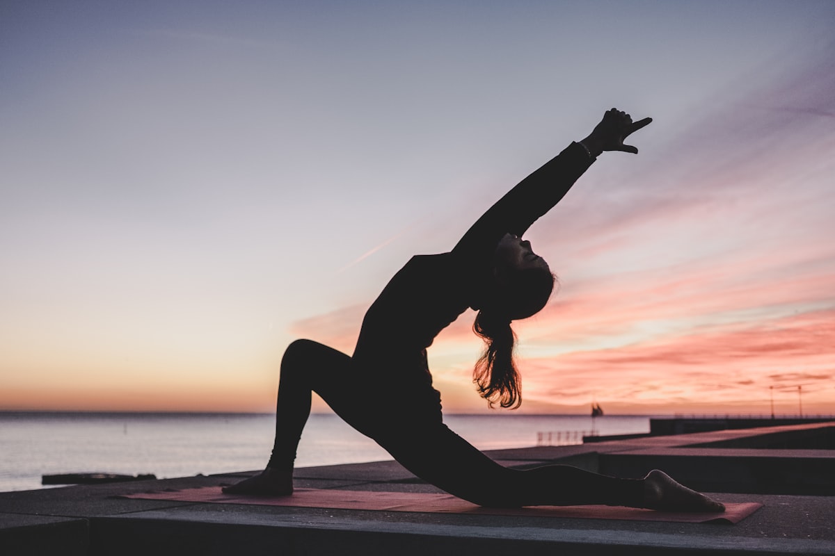Yoga warrior pose at sunset by the water - Yunique Medical
