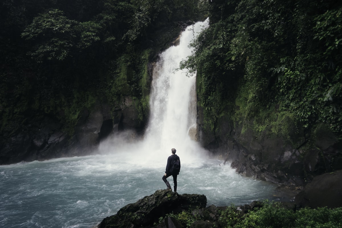 Lone figure gazing at a cascading waterfall surrounded by lush nature - Yunique Medical