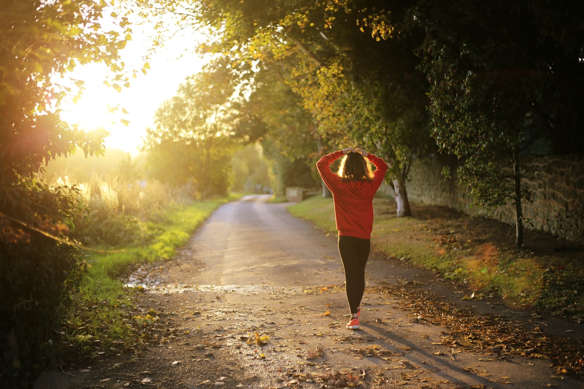Woman jogging down a tree-lined path in golden morning light - Yunique Medical