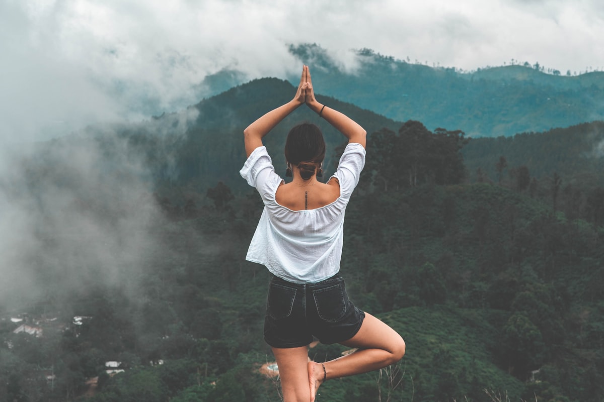 Woman in tree pose overlooking misty mountains - Yunique Medical