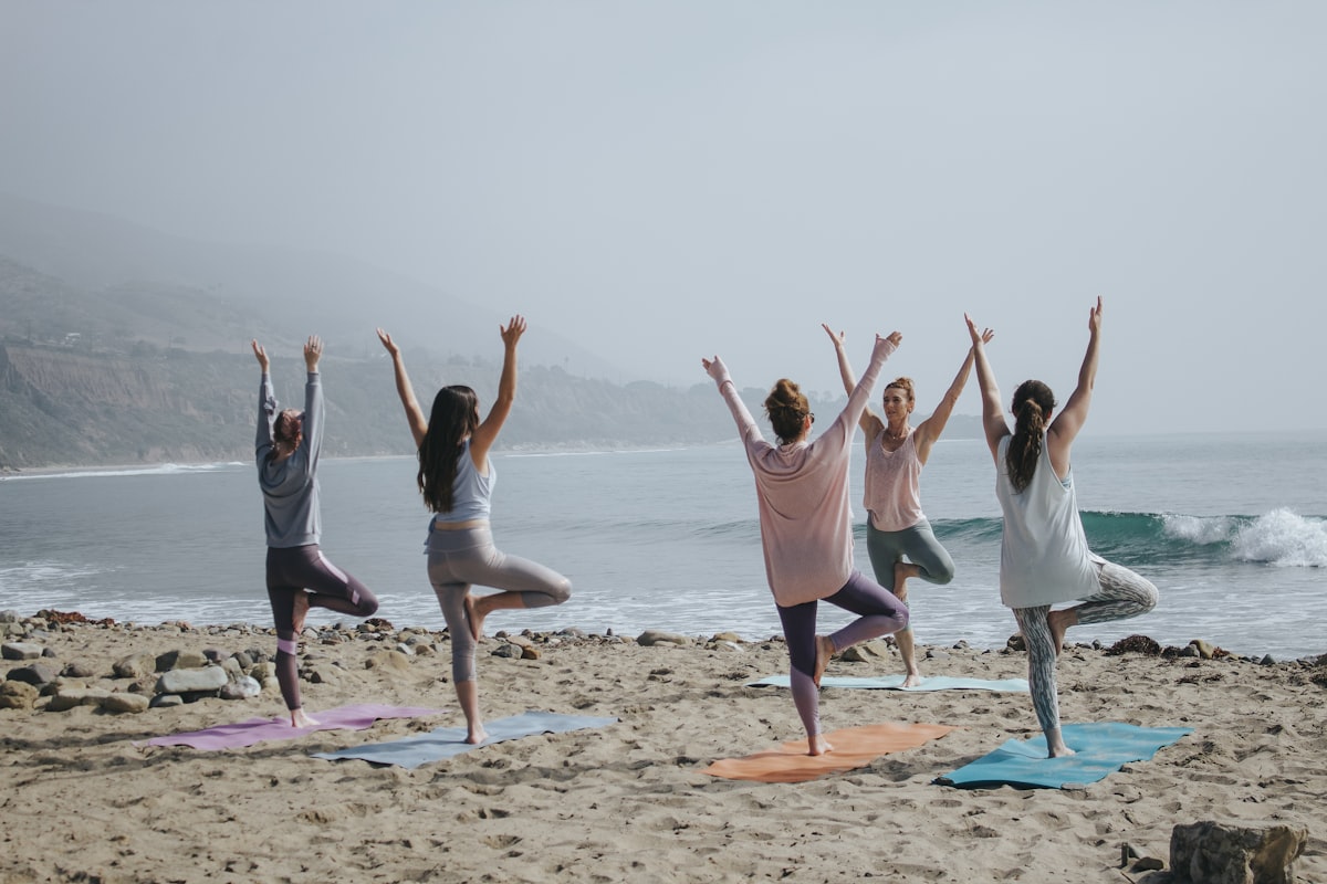 Group of women practicing yoga on the beach - Yunique Medical
